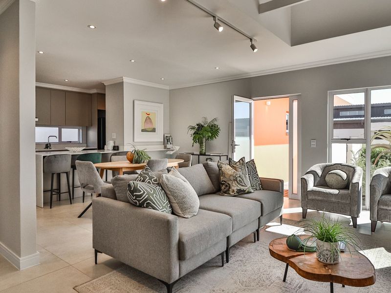 Modern open-plan living area featuring a seamless flow between the lounge and kitchen, enhanced by recessed lighting and neutral tiled flooring.