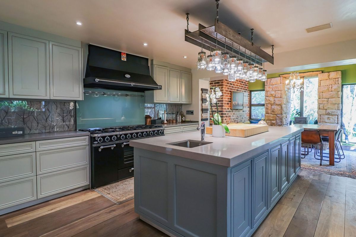 A modern, well-appointed kitchen featuring a large central island, high-end built-in oven, stone countertops, and elegant pendant lighting with hardwood flooring throughout.