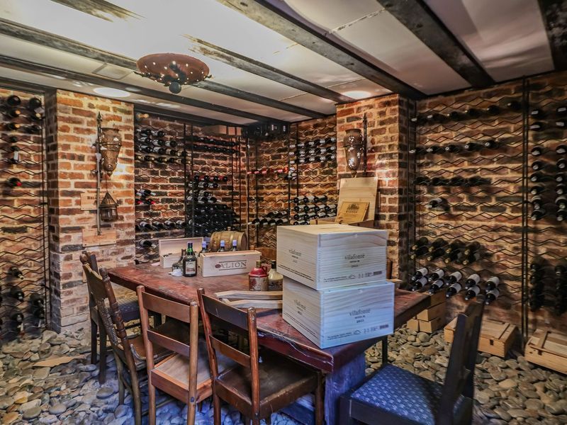 A rustic wine cellar featuring exposed brick walls, timber ceiling beams, and extensive built-in wine racking with a unique pebble floor finish.