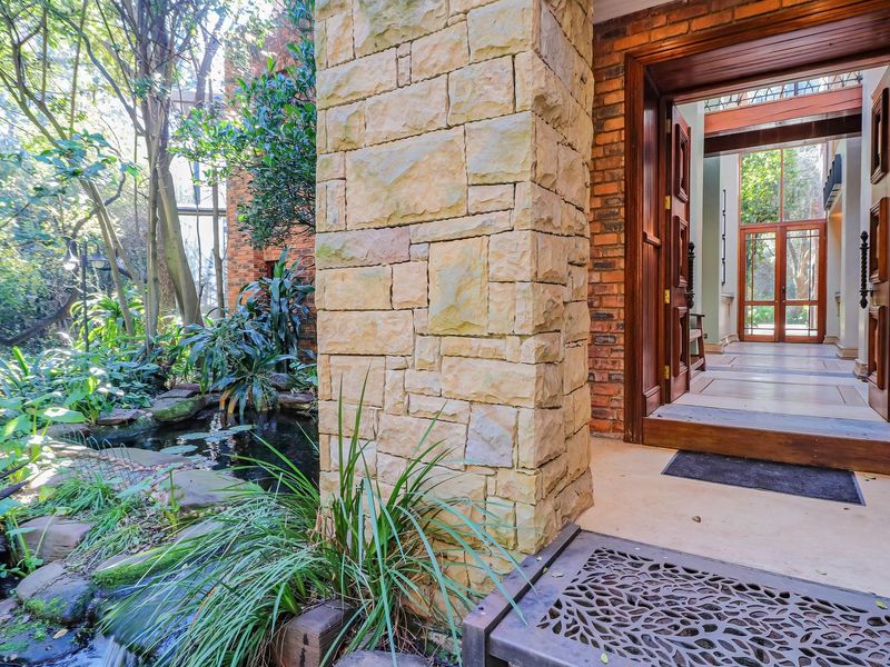 A grand entrance featuring natural stone cladding, exposed brickwork, and a timber door frame, overlooking a tranquil garden water feature.