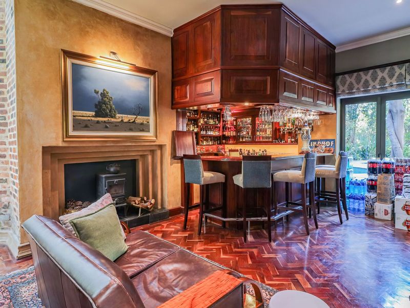 A sophisticated home bar area featuring a custom wooden bar counter, a cozy wood-burning fireplace, and elegant herringbone parquet flooring with garden views.