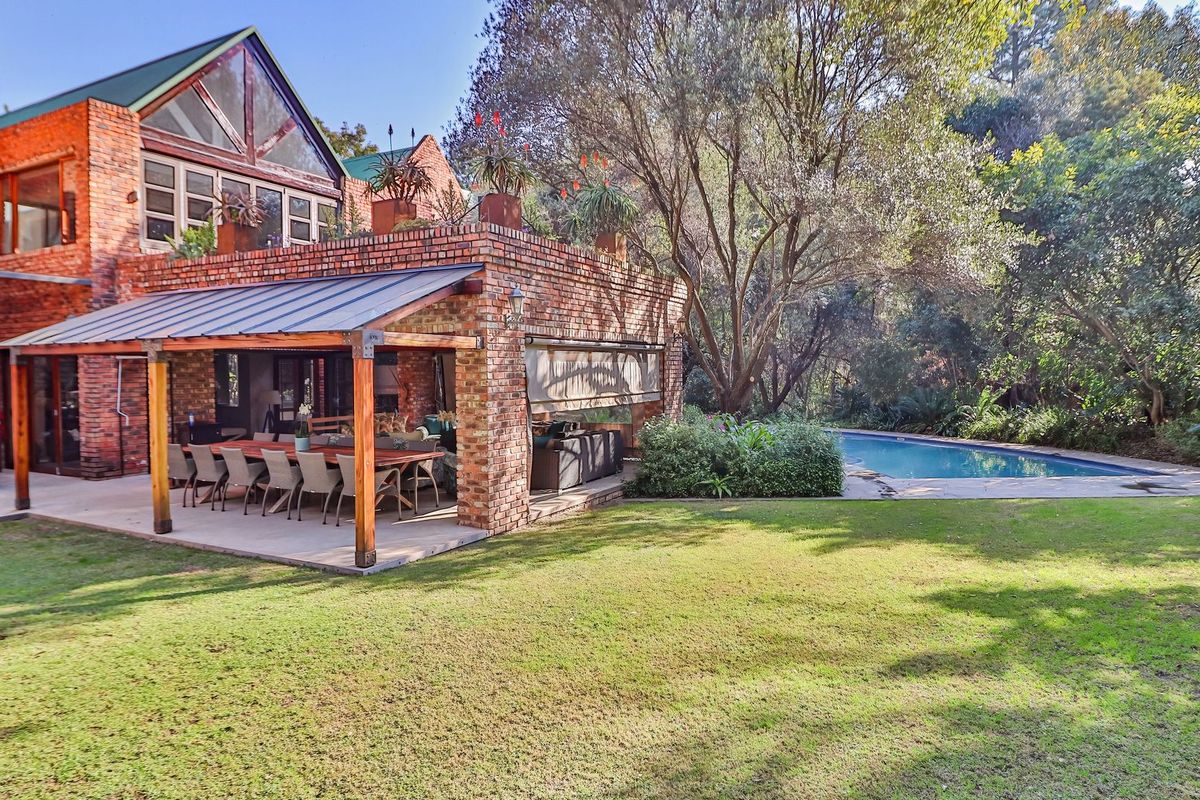 Spacious rear exterior featuring an exposed brick facade, a large covered patio area, a swimming pool, and a well-maintained garden setting.