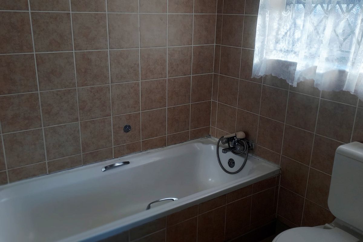 A functional bathroom featuring a standard bathtub, toilet, and neutral ceramic wall and floor tiling.