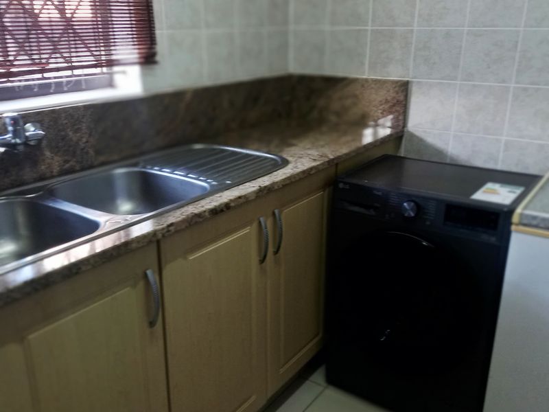 A functional scullery area featuring granite countertops, double stainless steel sink, and built-in cabinetry with tiled wall finishes.