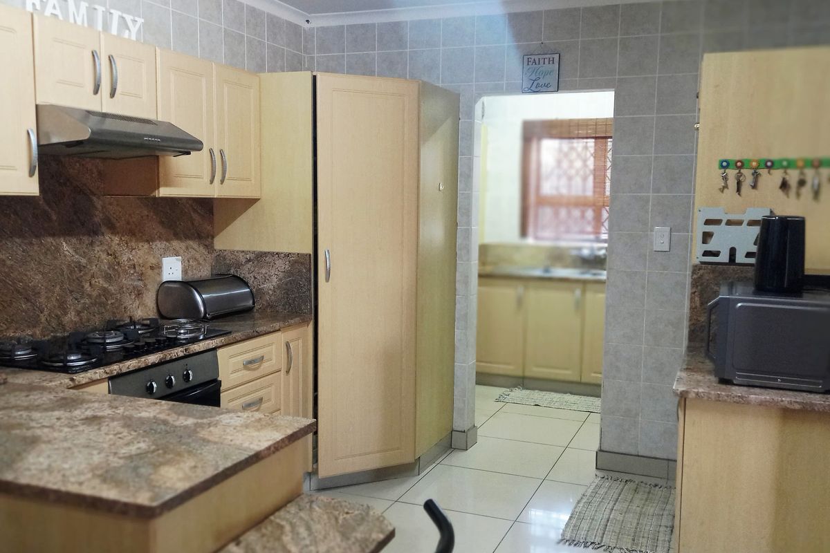 A functional kitchen featuring light wood cabinetry, granite countertops, a gas hob with extractor, and tiled finishes, with an adjacent scullery area visible.