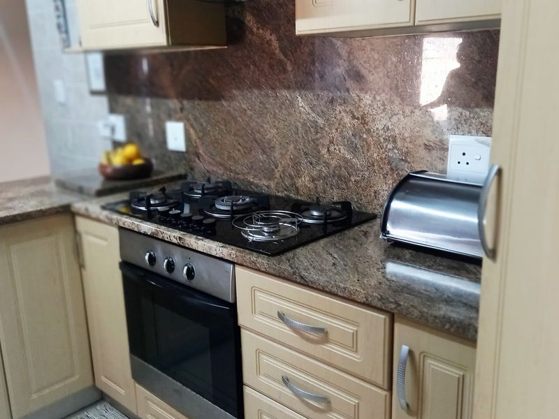 A functional kitchen featuring light-toned cabinetry, granite countertops, a gas hob, and a built-in oven with an overhead extractor fan.