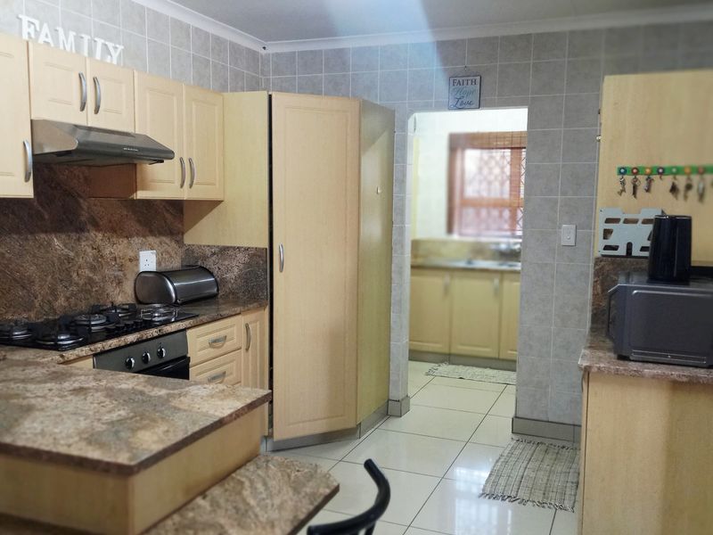 A functional kitchen featuring light wood cabinetry, granite countertops, a gas hob with extractor, and tiled finishes, with an adjacent scullery area visible.
