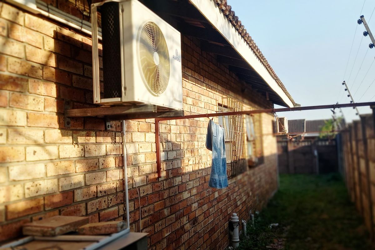 Rear exterior view of the property featuring exposed brickwork, a mounted air conditioning unit, and perimeter electric fencing.