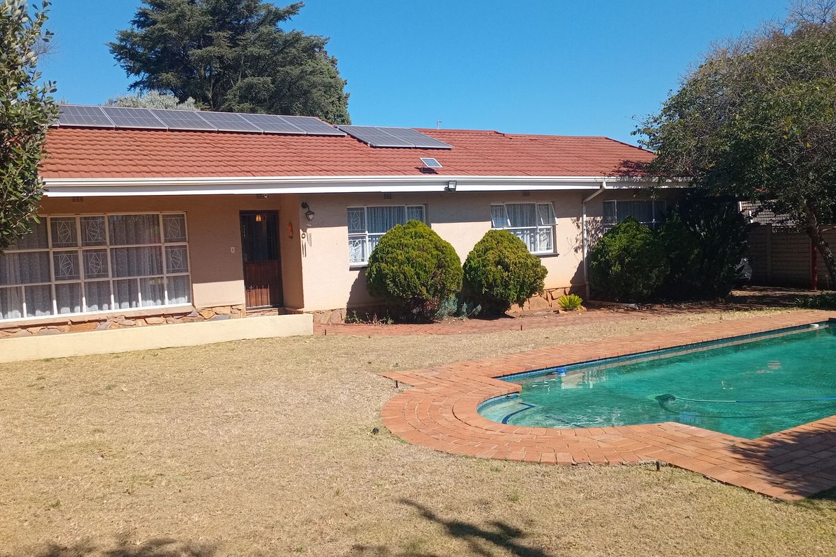Rear view of the house featuring a swimming pool with brick coping, a tiled roof with installed solar panels, and established garden landscaping.