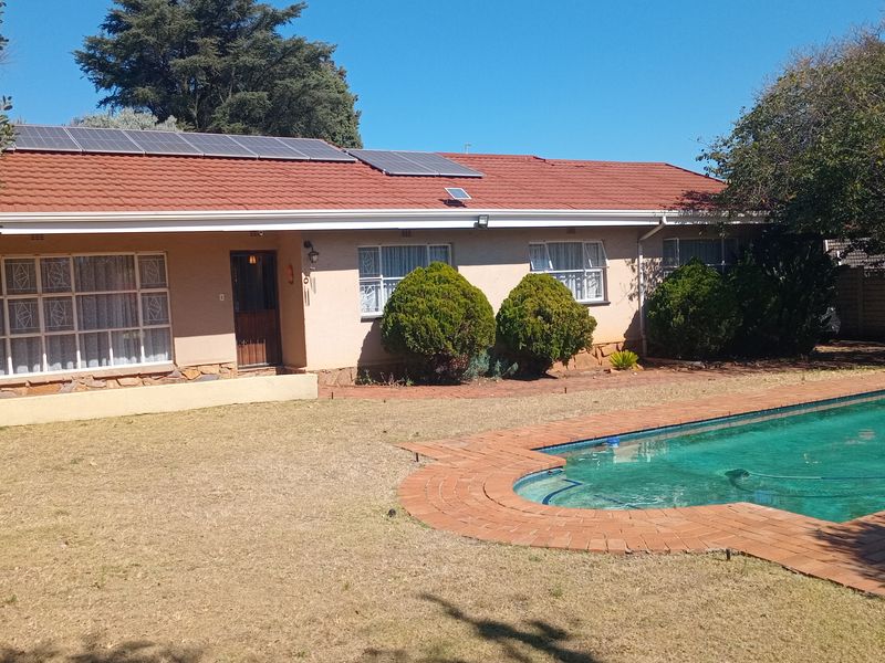 Rear view of the house featuring a swimming pool with brick coping, a tiled roof with installed solar panels, and established garden landscaping.