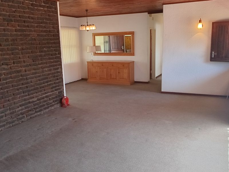 Spacious living area featuring an exposed brick feature wall, timber ceiling, and neutral carpeting, offering a dated but functional layout ready for modernization.