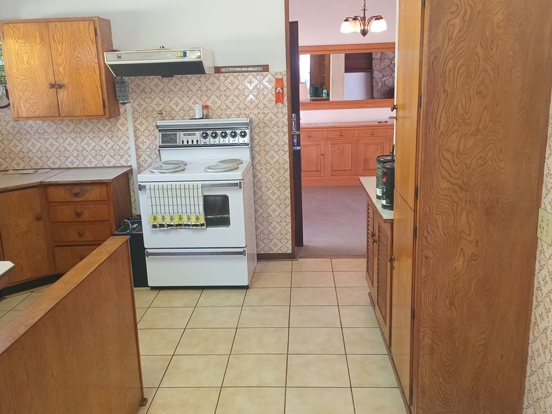A dated kitchen featuring wooden cabinetry, tiled backsplash, and a freestanding electric stove, offering potential for a modern renovation.