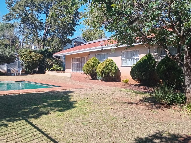 Rear view of the property featuring a swimming pool, brick paved patio area, and established garden surroundings.