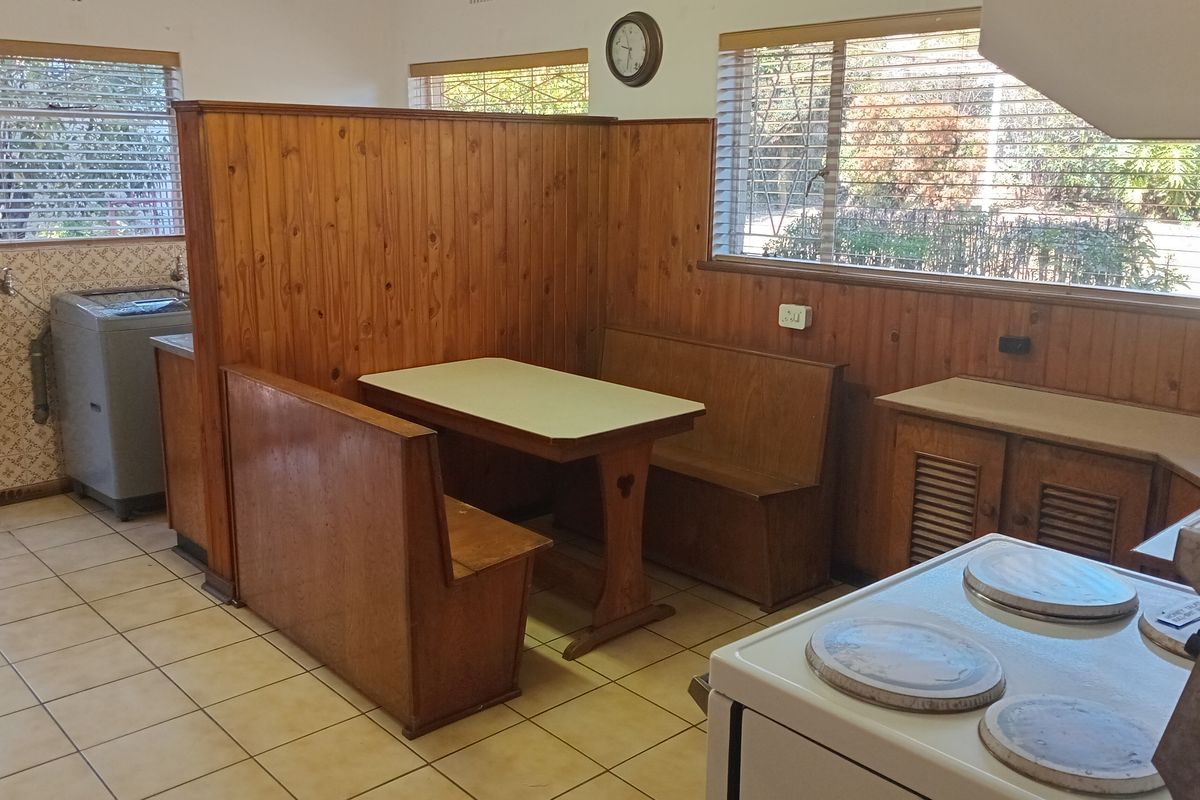 A dated kitchen featuring built-in wooden breakfast nook seating, tiled flooring, and traditional cabinetry, offering potential for a modern renovation.
