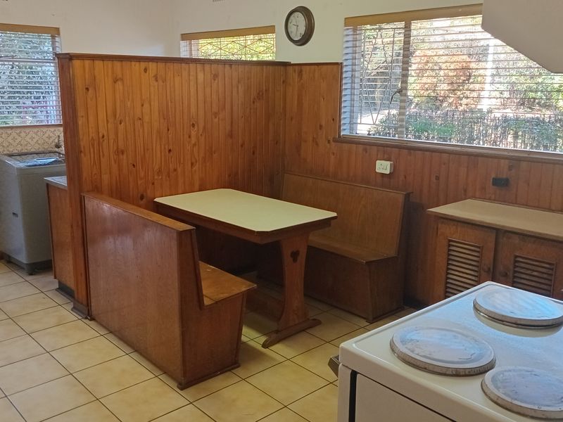 A dated kitchen featuring built-in wooden breakfast nook seating, tiled flooring, and traditional cabinetry, offering potential for a modern renovation.