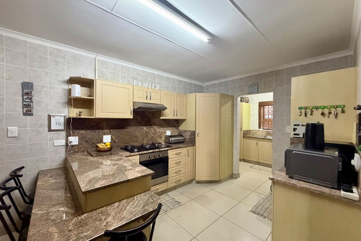 Functional kitchen featuring granite countertops, built-in cabinetry, gas hob, and oven, with an adjoining scullery area and tiled finishes throughout.