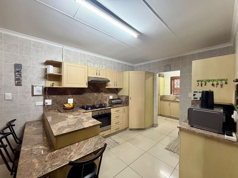 Functional kitchen featuring granite countertops, built-in cabinetry, gas hob, and oven, with an adjoining scullery area and tiled finishes throughout.