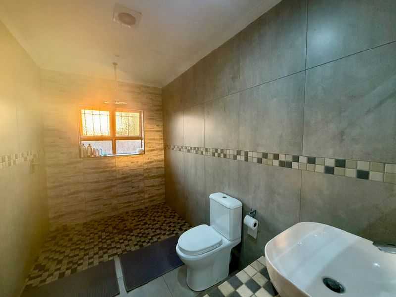 A modern bathroom featuring large format wall tiles, a contemporary basin, and a toilet, with natural light streaming through the window.