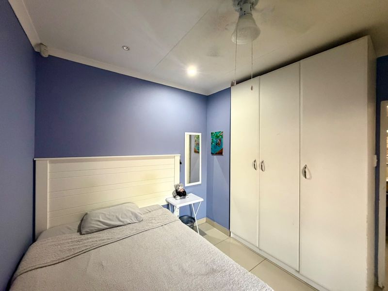 A bedroom featuring blue walls, tiled flooring, a built-in wardrobe, and a ceiling fan.