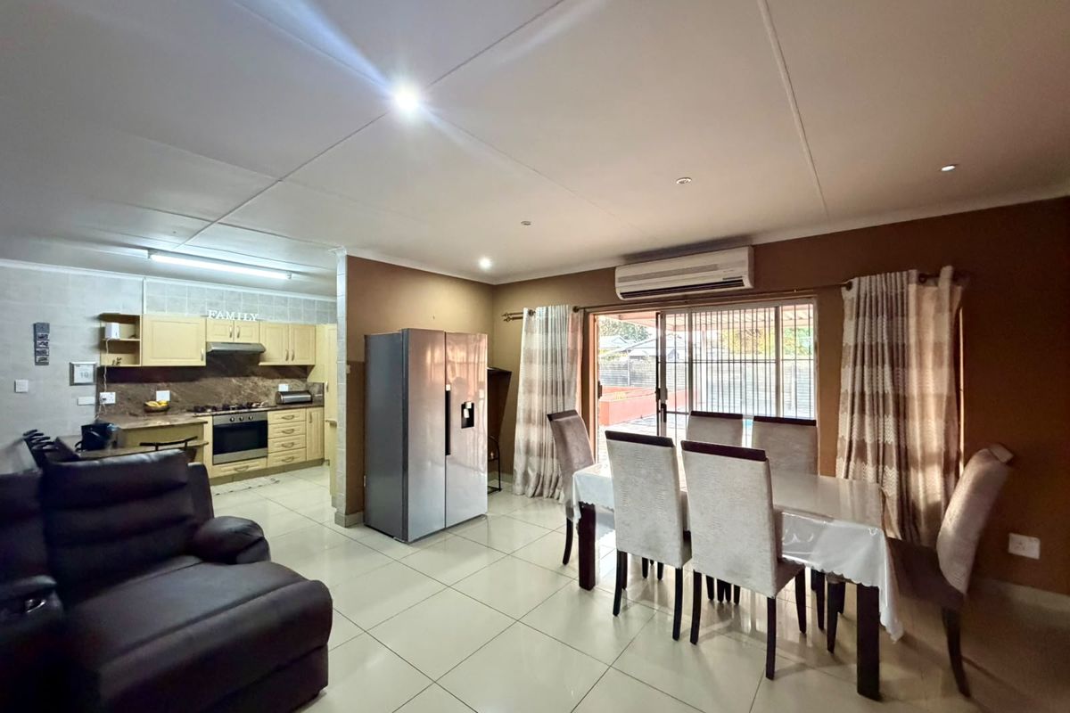 Open-plan living and dining area featuring tiled floors, a split-system air conditioner, and a functional kitchen with built-in cabinetry and appliances.