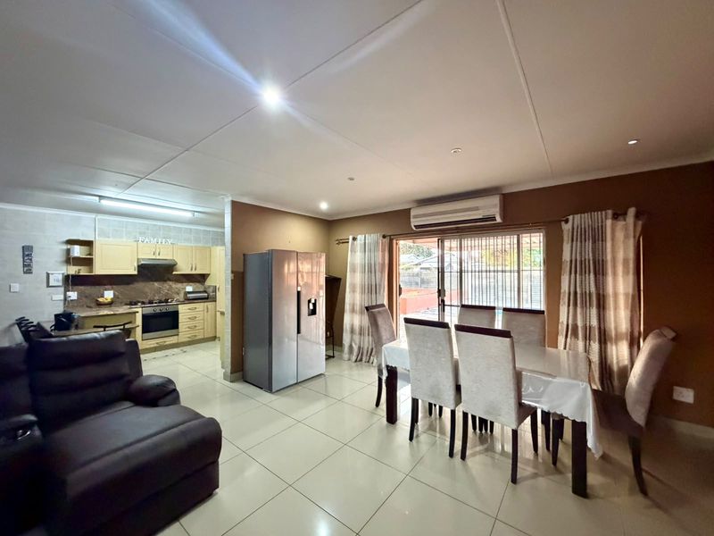 Open-plan living and dining area featuring tiled floors, a split-system air conditioner, and a functional kitchen with built-in cabinetry and appliances.