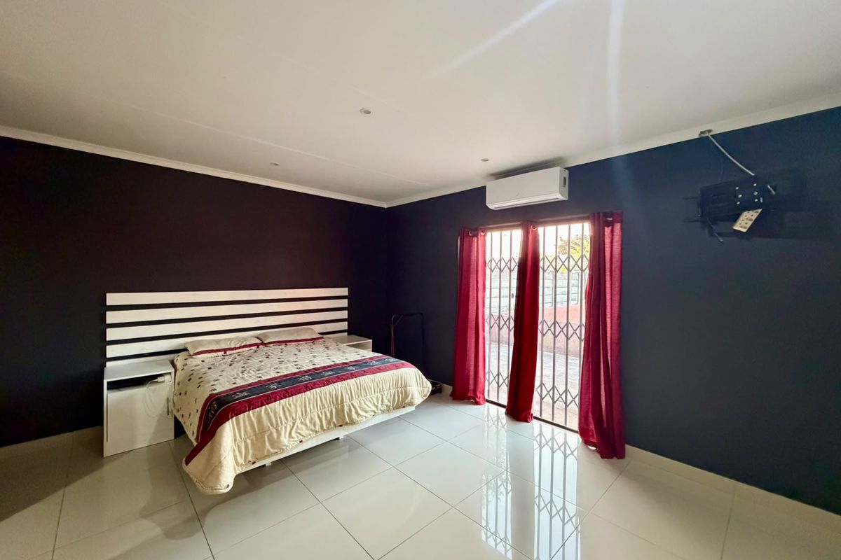 Spacious bedroom featuring polished tiled flooring, dark accent walls, a wall-mounted air conditioning unit, and direct access to the exterior via a security gate.