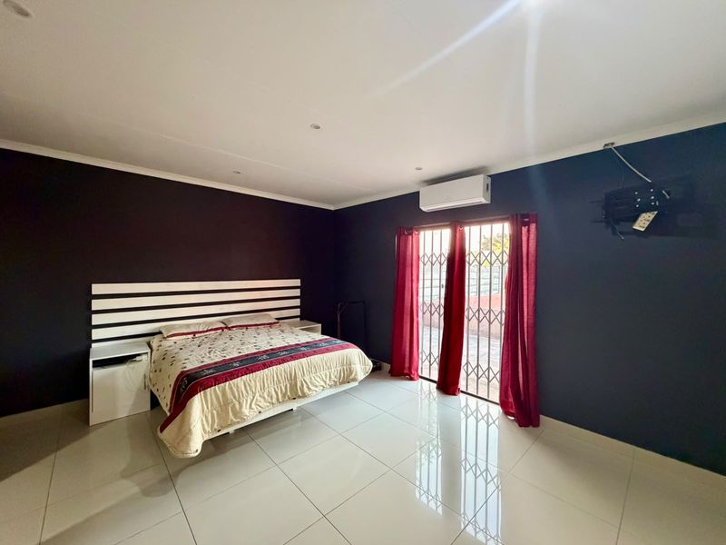 Spacious bedroom featuring polished tiled flooring, dark accent walls, a wall-mounted air conditioning unit, and direct access to the exterior via a security gate.