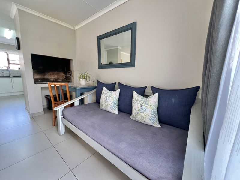 A covered patio area featuring a built-in braai, neutral tiled flooring, and direct access to the kitchen area.