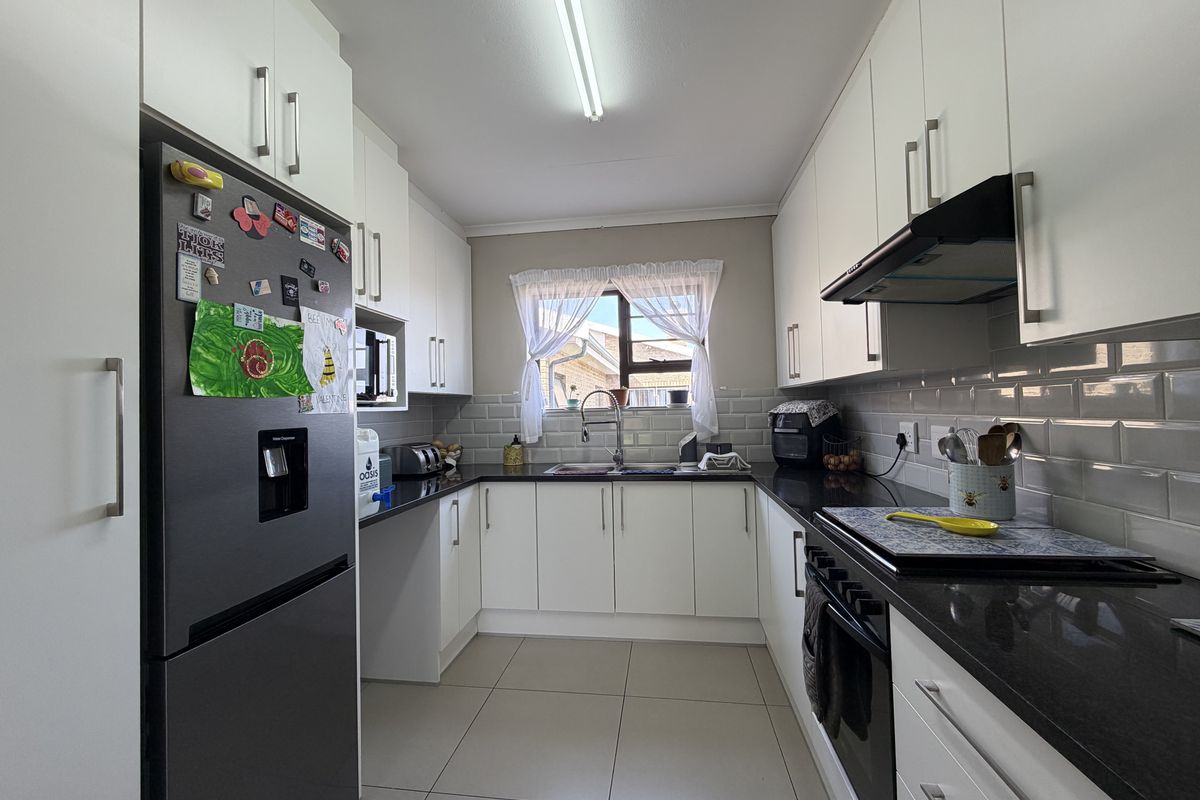 A well-maintained kitchen featuring white cabinetry, dark granite countertops, subway tile backsplash, and integrated appliances including an oven and extractor fan.