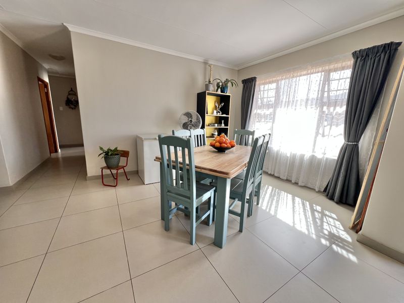 A bright and spacious dining area featuring large windows, neutral wall tones, and clean tiled flooring, offering a comfortable space for family meals.