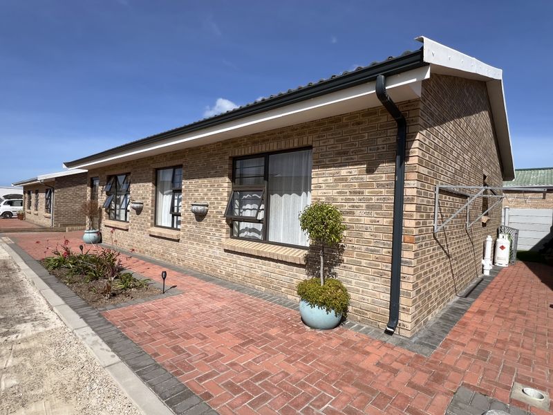 A well-maintained townhouse exterior featuring face brick construction, tiled roofing, aluminium window frames, and neat paved surrounds.