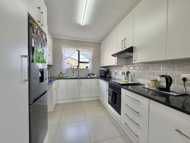 A well-maintained kitchen featuring white cabinetry, dark granite countertops, subway tile backsplash, and integrated appliances, offering a clean and functional workspace.