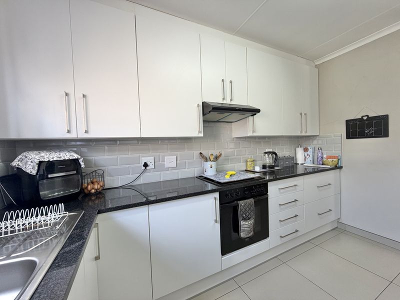 A well-maintained kitchen featuring white cabinetry, black granite countertops, a subway tile backsplash, and integrated oven with extractor fan.