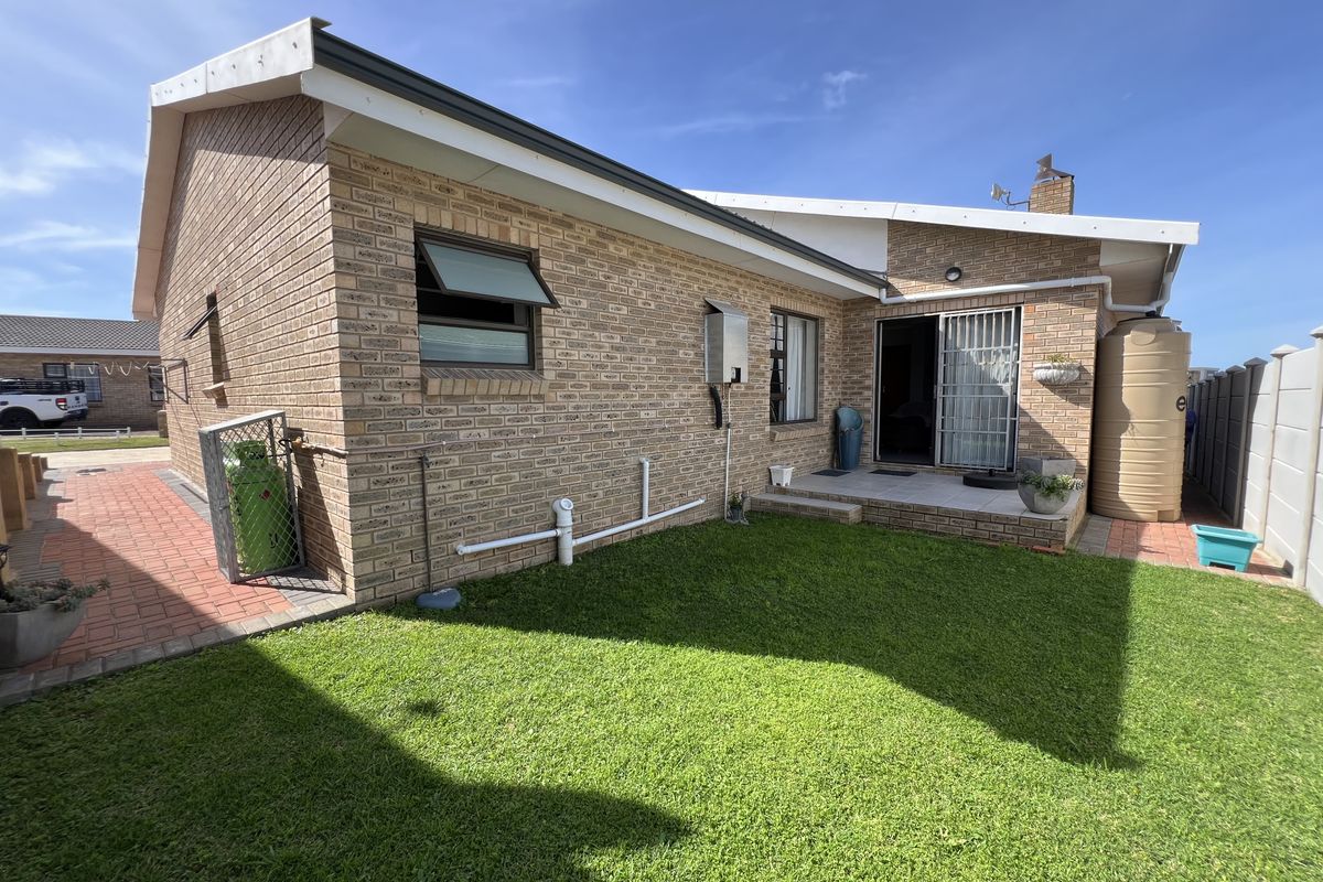 Rear view of the townhouse featuring a face brick facade, a small paved patio, a lawn, and a water storage tank.