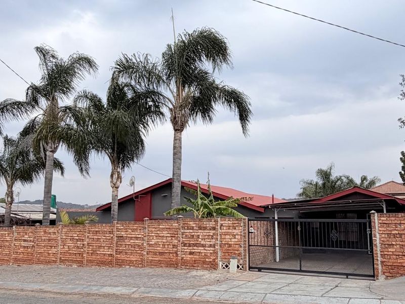 Front view of the property featuring a brick boundary wall, metal driveway gate, carport, and a red metal roof.