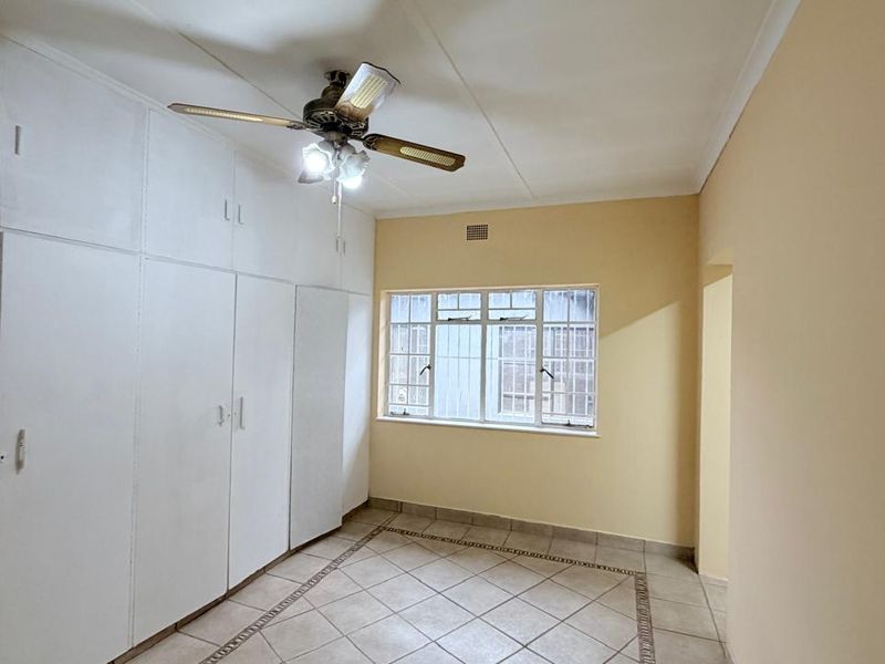 A spacious, empty bedroom featuring extensive built-in cupboards, tiled flooring, and a ceiling fan, offering a clean canvas for personalization.