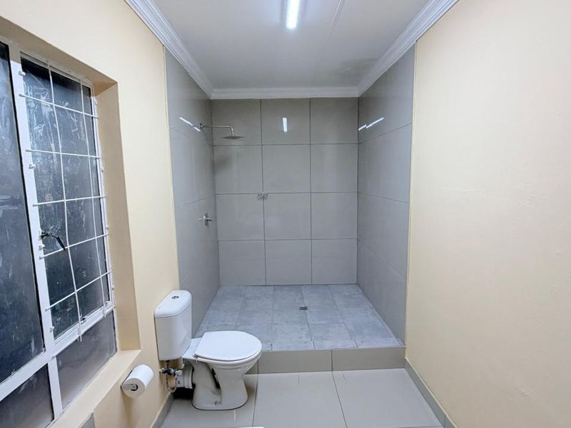 A functional bathroom featuring a walk-in shower with a rain shower head, tiled walls and flooring, and a standard toilet.