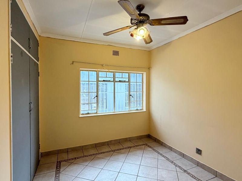 A vacant bedroom featuring tiled flooring, built-in cupboards, and a ceiling fan, offering a blank canvas for personalization.