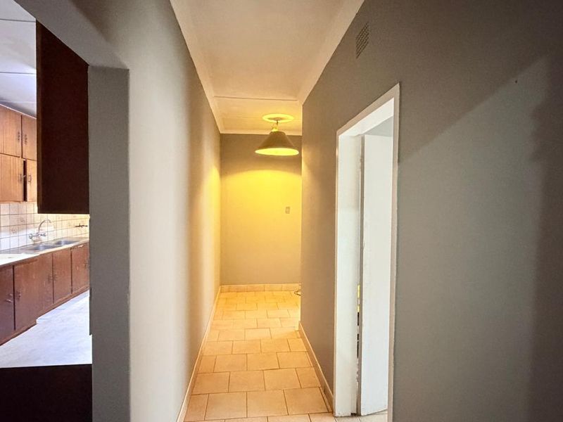 A clean, neutral hallway with tiled flooring leading towards a kitchen area featuring wooden cabinetry and tiled splashbacks.