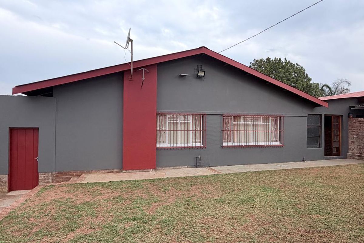 Rear view of the house featuring a grey facade with red accents, security bars on windows, and a well-maintained lawn area.
