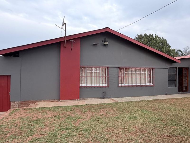 Rear view of the house featuring a grey facade with red accents, security bars on windows, and a well-maintained lawn area.