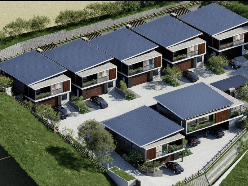 An aerial view of a modern residential complex featuring multiple units with pitched roofs, private garages, and paved driveway access.