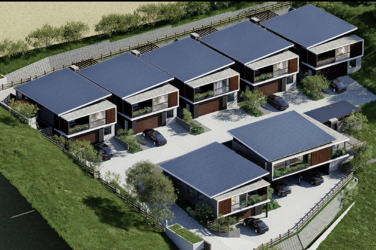 An aerial view of a modern residential complex featuring multiple units with pitched roofs, private garages, and paved driveway access.