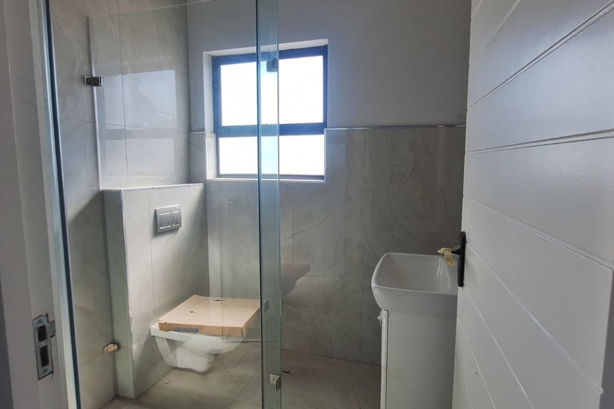 A modern, compact bathroom featuring a wall-hung toilet with a concealed cistern, a pedestal basin, and a glass-enclosed shower area.