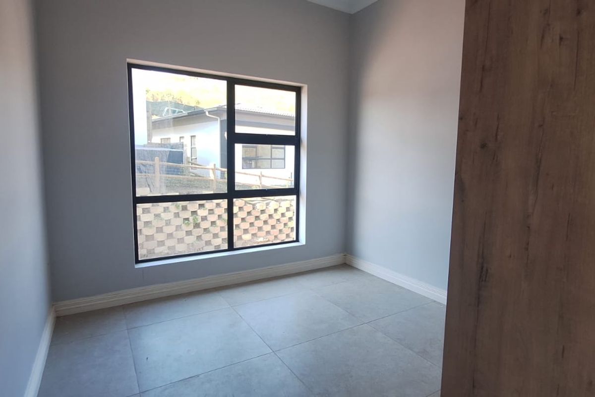 A bright, empty bedroom featuring modern neutral wall paint, large aluminium-framed windows, and clean tiled flooring.