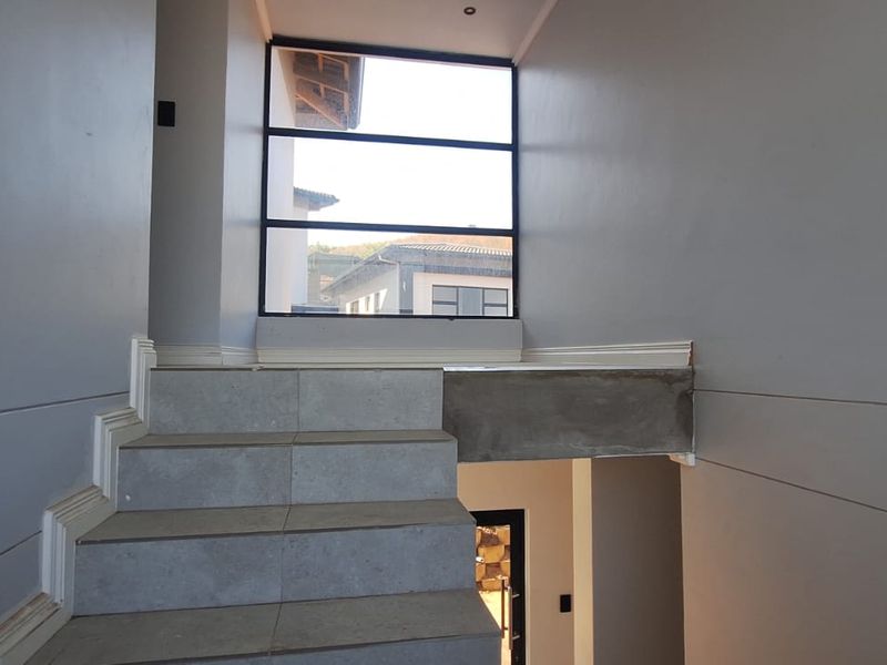 A modern staircase area featuring tiled steps, large windows providing natural light, and clean wall finishes, currently awaiting final finishing touches on the landing.