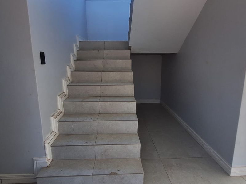 A vacant hallway featuring a tiled staircase and neutral wall finishes, providing a clean canvas for interior design.