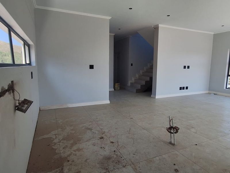 An open-plan living area in a new build, featuring tiled floors, recessed lighting, and a staircase, currently in an unfinished state.