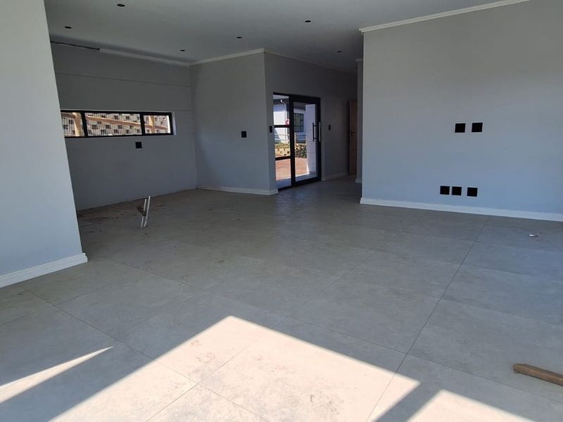 Spacious, open-plan living area featuring large format floor tiles, modern aluminium window frames, and recessed downlighting, currently in a near-complete state.