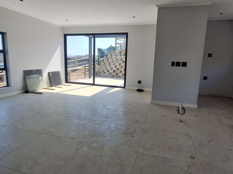Spacious open-plan living area featuring large format floor tiles, modern aluminium sliding doors, and expansive windows with views, currently in an unfinished state.